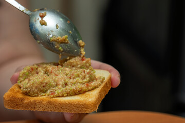 Large metal spoon spreads guacamole onto toast during a homemade lunch, capturing a simple and delicious meal moment