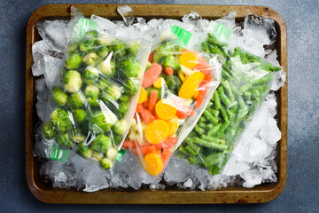 Frozen vegetables in plastic bags lie on ice. Top view. Food preparation for the winter.
