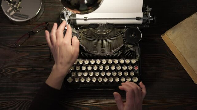 Hands of writer typing text on vintage typewriter keyboard in home office at desk, top view
