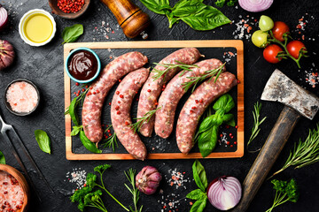 Raw beef sausages with rosemary and spices, ready to be grilled. On a wooden cutting board. Close...