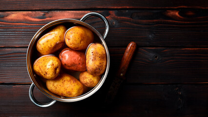 Potatoes with peel in a stainless steel pot with boiling water. Cooking dishes from potatoes. On a wooden background. Free space for text.