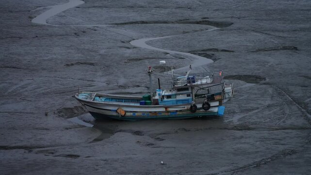 Old fishing boat standing on the mudflat. Drone view angle of empty muddy surface with boat left on it at Sunset time.