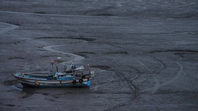 Old fishing boat standing on the mudflat with Wide Angle. High angle of empty muddy surface with boat left on it at Sunset time.