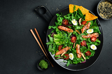 Fresh healthy salad. Salad with arugula, salted salmon, avocado, quail eggs and mushrooms. In a black plate. Diet food.