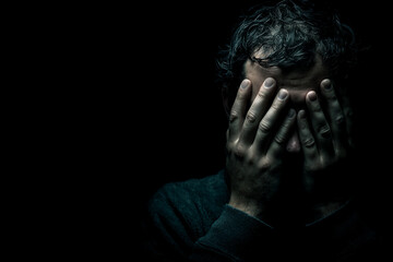 Dark image of man's face hidden by hands, conveying feelings of despair, stress, or anxiety, suitable for mental health awareness campaigns