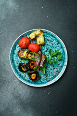 Grilled vegetables on a blue round plate. On a black stone background.