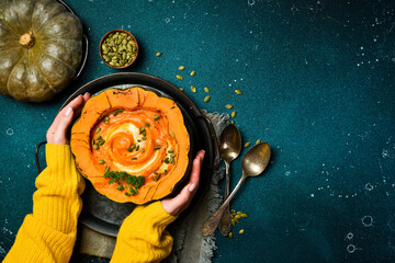 Female hands hold Pumpkin cream soup with pumpkin seeds cooked in a pumpkin. Dietary nutrition. Top view.