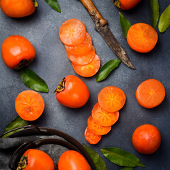 Sliced ​​and whole persimmon fruits on a gray stone table. Top view. Autumn seasonal fruits.