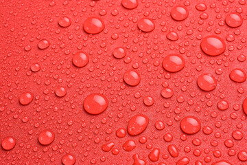 Textured red surface with clear water splashes, background for design or text. Top view. Free space.