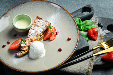 A piece of sweet poppy seed cake with a scoop of ice cream and cream. Close up. on a plate On a black stone background.