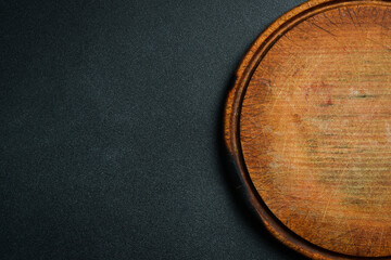 Kitchen round cutting board. Brown board. Kitchen utensils. On a dark background.