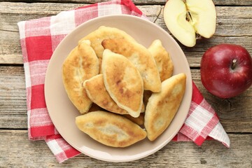 Delicious fried pyrizhky (stuffed pies) and apples on wooden table, flat lay