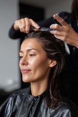 Fototapeta premium A woman is getting her hair done by a stylist. The stylist is using a comb to style the woman's hair. The woman is smiling and she is enjoying the experience