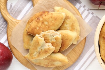 Delicious fried pyrizhky (stuffed pies) and apples on white wooden table, flat lay