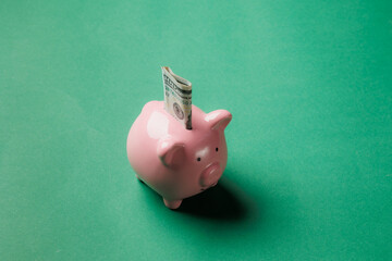 Piggy bank shown with cash inserted on green background displays the importance of saving money for...