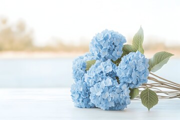 A bouquet of light blue hydrangeas rests on a white wooden surface against a blurred outdoor background