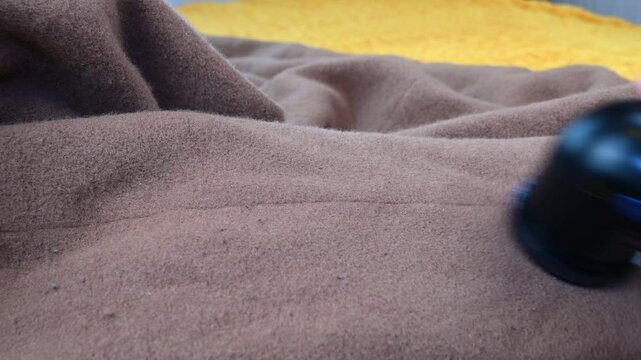 Hand removing lint from blanket with electric fabric shaver  satisfying textile care.