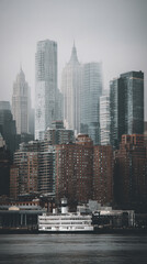 Misty cityscape view featuring numerous skyscrapers and a ferry boat, showcasing urban architecture and transportation, creating a calm, atmospheric scene