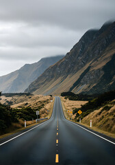 Scenic Asphalt Road Through Mountains and Green Fields Under Cloudy Sky