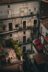 Old residential buildings with rustic balconies, air conditioners, and rooftop terraces in Catania, Sicily, Italy. Moody urban atmosphere with Mediterranean charm.