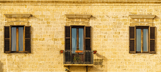 old yellow facade of house with three brown vintage wooden windows in retro italian european style