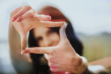 In a lively outdoor location, a fashionable young girl strikes a playful pose, framing herself with her hands