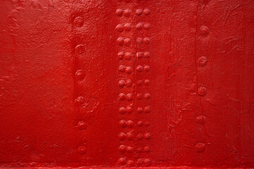 A closeup view of an industrial red painted metal surface with symmetrical rows of rivets,...