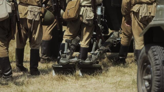 Reenactment portrays Soviet forces during Great Patriotic War. Participants stand near field artillery 82mm mortar, likely BM-37 model piece WWII era. Men wear authentic Red Army uniforms boots