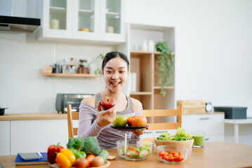 Smiling woman in a modern kitchen with fresh fruits, veggies, blender, and juice, embracing clean...