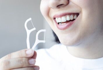 A young woman smiling and holding dental floss. Dental healthcare and orthodontic concept