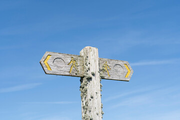Traditional wooden sign with symbols for a walker and directional arrow showing the way in yellow...