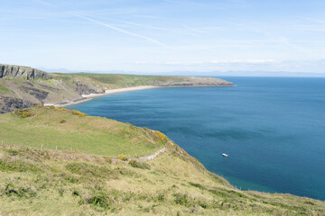 Green grass fields lead to a coastal bay with a blue sea  and sandy Porth Ceiriad Beach in the distance on a sunny day on the Lleyn Peninsular, Wales, UK.