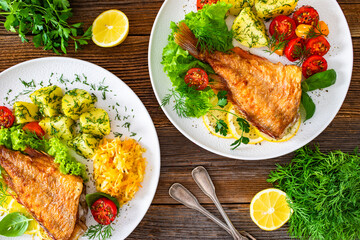 Fried atlantic redfish with boiled potatoes and tomato salad on wooden table