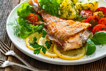 Fried atlantic redfish with boiled potatoes and tomato salad on wooden table