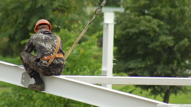 A male fitter at a construction site assembles a metal structure at a construction site in the summer. Danger at height, copy space for text