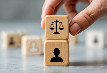 Hand stacking wooden cubes with justice scale and person icons, symbolizing legal system and human rights concepts, close-up view