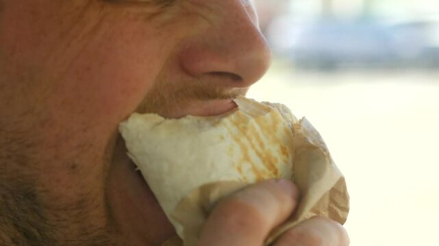 Man driver consumers greasy shawarma in car. Unhealthy fast food shawarma meal promotes poor nutrition habits with processed meat and fatty sauces in cramped vehicle space. Unhealthy shawarma food. 
