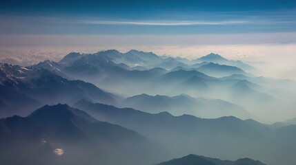 Fototapeta premium Aerial view of misty mountains with soft blue and white sky hues, peaks standing out against foggy background, creating an ethereal natural landscape atmosphere.