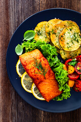 Seared salmon steak with cherry tomato salad and fried potato slices on wooden table	