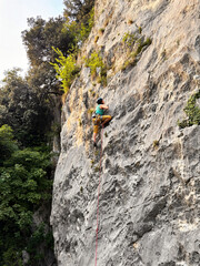Obraz premium Female Climber Leading A Route In Yellow Pants At Nago Rock Climbing Area Near Arco, Lake Garda, Italy