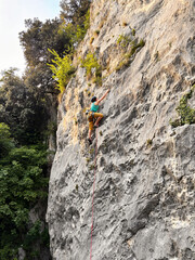 Female Climber Leading A Route In Yellow Pants At Nago Rock Climbing Area Near Arco, Lake Garda, Italy