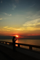 Silhouette of people standing alone and holding to mobile phone for play and update online news in the evening time at sunset down. Majestic sunset cloudscape.