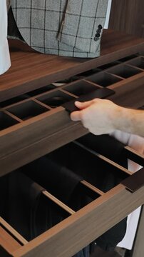Close-up of a hand opening a wooden drawer in a wardrobe with things, modern interior.Vertical video