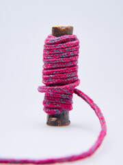 Close-up of pink and gray wool yarn neatly wrapped around a natural wooden stick against a white background. Represents crafting, knitting, and textile materials in a minimalistic style.