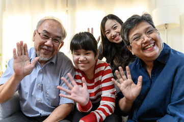 POV video call greeting with happy multi-generation Asian family smiling and waving together at home, representing love, connection, and diversity in modern family lifestyle. Family selfie video call.