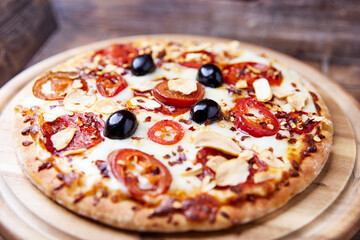 Pizza with salami and mozzarella cheese, jalapeno pepper and black olives. Wooden background. Soft focus.	
