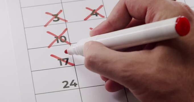 Close-up of a hand marking off dates in a calendar using a red marker. Concept of time management, scheduling, and countdown. Hand Crossing Off Dates On Calendar With Red Marker Pen