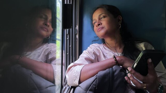 A happy woman sitting inside a train and listening music using mobile phone
