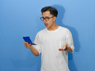 Portrait of a confused young Asian man in a white t-shirt, showing a shocked expression while...