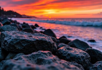 Obraz premium Vibrant sunset over rocky shoreline with colorful sky and ocean waves